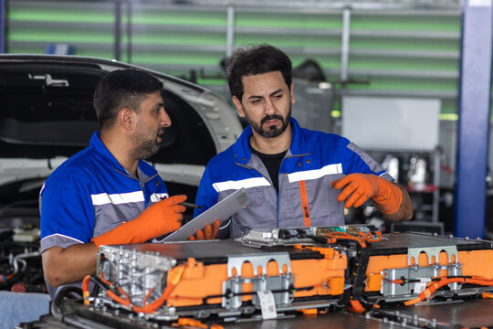 EV battery service concept, two technicians using tablet while inspecting electric vehicle battery modules in workshop. EV, battery, technician, teamwork, maintenance.