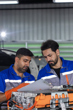 EV battery service concept, two technicians using tablet while inspecting electric vehicle battery modules in workshop. EV, battery, technician, teamwork, maintenance.
