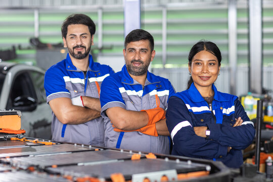 Confident automotive technician team standing beside an electric vehicle battery pack in EV workshop, representing skilled workforce, teamwork, engineering, professional service.