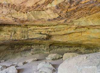 Interior of a sandstone rock shelter with layered ceiling and scattered boulders © Kit Leong