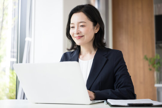 ノートパソコンで仕事をする女性会社員、オフィスで笑顔で働くビジネスウーマンのデスクワーク
