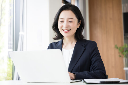 ノートパソコンで仕事をする女性会社員、オフィスで笑顔で働くビジネスウーマンのデスクワーク