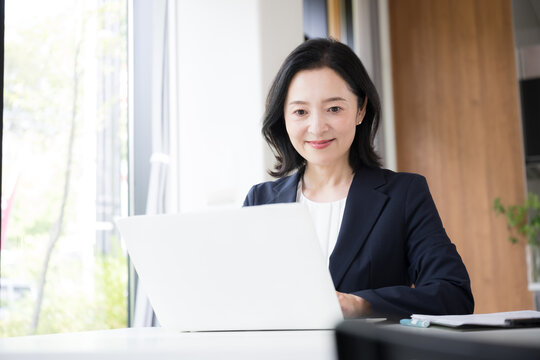 ノートパソコンで仕事をする女性会社員、オフィスで笑顔で働くビジネスウーマンのデスクワーク