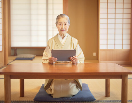 Senior japanese woman in kimono sitting in traditional tatami room using digital tablet for telehealth