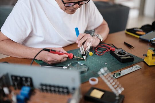 Close-up, man's hand repairs home electrical appliance, disassembling and soldering circuit board, focusing on precision detail, DIY fix tools, electronics component workshop hobby, expert handyman.