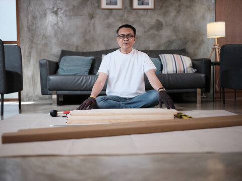 Portrait of Asian mature man preparing flat-pack furniture parts, cheerful smile, self-assembly with carpentry diy tools, home improvement, craft install hobby workshop, handyman active lifestyle.