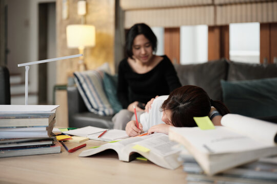 Two College Asian friends, teenage girl tired and burned out from overwhelmed homeschooling, study pile of books, stressed learning at home, her friend wakes up while napping, education exam support.