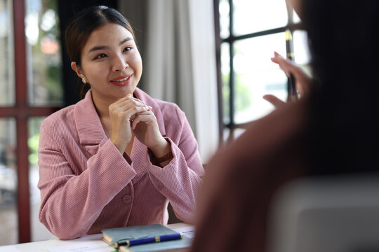 Asian businesswoman listening to colleague explaining project during meeting.