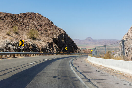 Curving asphalt road winds through rugged desert mountains with yellow traffic signs under a clear blue sky, Interstate-8 in Fortuna Foothills, Arizona