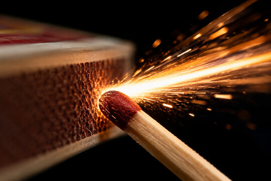 A single matchstick against the striking strip, a bright spark trail.