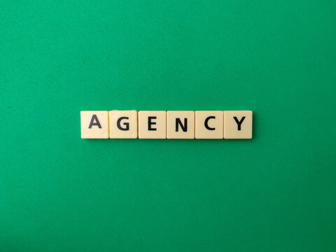 Square beige letter tiles form the word AGENCY in a straight horizontal line over a solid green background