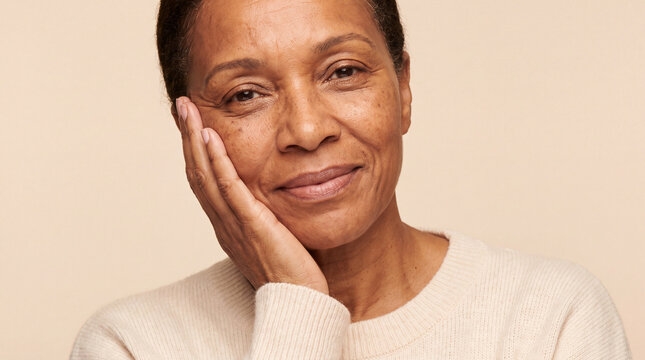 National Healthy Skin Month portrait of a mature Black woman gently touching her cheek, great for age-inclusive beauty editorial and skincare website imagery.