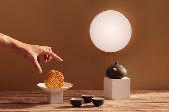 Cropped hand reaching for mooncake during Mid-Autumn Festival with full moon glow