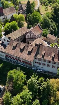 Drone view of Schloss Laufen and the Reformed Church of Laufen am Rheinfall, showing historic tiled roofs and wooded grounds above Rhine Falls in Switzerland.