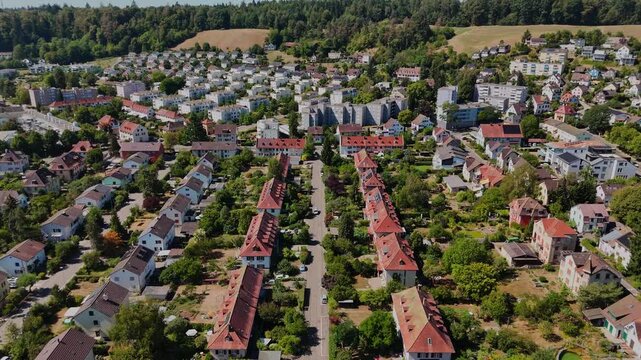Aerial view over a planned Swiss residential district with red-roofed row homes, apartment blocks, private gardens and tree-lined streets on a sunny summer day.