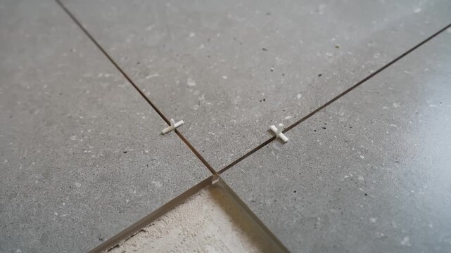 Close-up of cross spacers aligning gray floor tiles around an unfinished section, showing consistent grout gaps and adhesive beneath during installation.