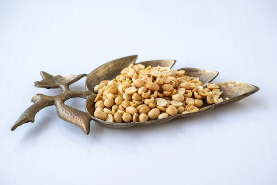 Roasted peeled peanuts served in a vintage leaf shaped brass tray isolated on white studio background, healthy crunchy snack concept.