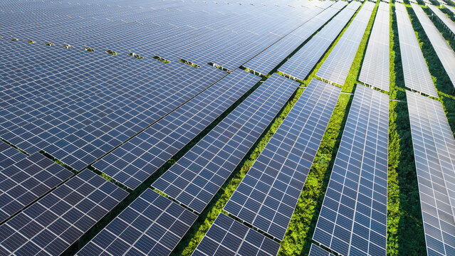 Aerial view of a large solar farm with rows of photovoltaic panels installed in a green field, capturing sustainable energy infrastructure