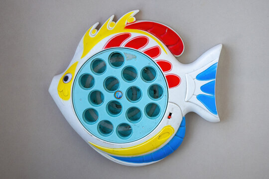 Top view of a colorful fish shaped plastic fishing game board toy isolated on plain grey surface, classic childhood arcade activity.