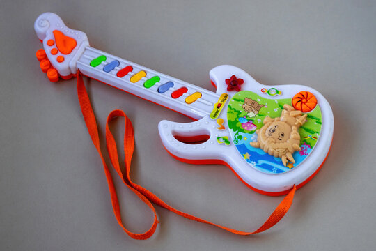 Childrens electronic toy guitar with cartoon animal graphics and colorful keys placed on plain neutral background.