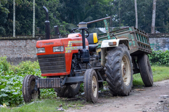Kishoreganj, Bangladesh - 03 September, 2026 - Front angle view of a stationary farm tractor coupled with a cargo trailer on a dirt ground.