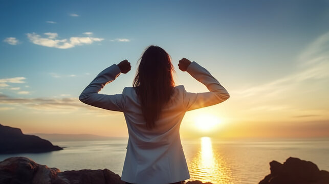 woman flexing arms at sunrise. Back view, full body of woman in business suit showing muscle and strength, with ocean and sun in background.