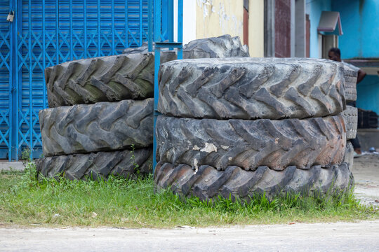 Close-up shot of massive worn tractor rubber tires piled up outside an auto repair store, discarded heavy machinery parts.