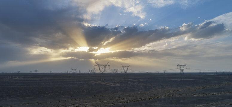 High-Voltage Transmission Towers Under Dramatic Sunbeams in Desert Gobi at Dusk