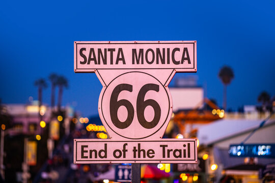 Route 66 end sign in Santa Monica. California Route 66 landmark with palm trees. Route 66 destination marker at the pier. Famous Route 66 sign against blue sky.