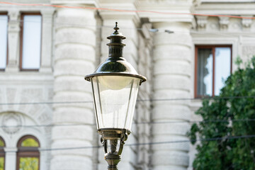 Lamp stands prominently. Facade forms background. Windows frame architecture. Foliage softens surroundings. © VladyslavShcherbakov