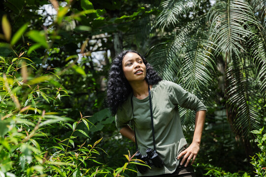 Woman Shading Her Eyes and Looking Up While Exploring a Tropical Garden