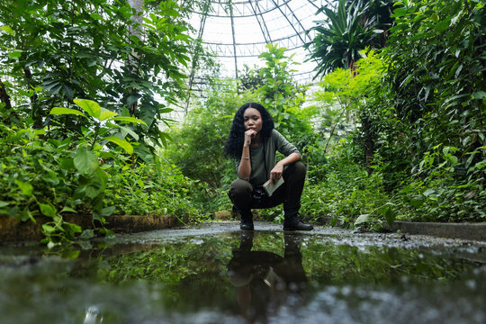 Thoughtful Woman Contemplating Nature Beside a Puddle in a Botanical Dome
