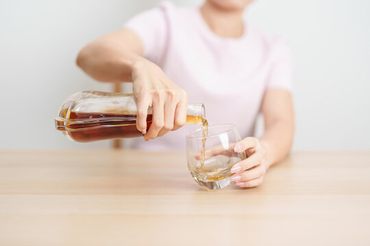 woman pour cognac into a glass on table, suffering from alcohol addiction, alcoholism concept. depicting emotional distress, depression, substance abuse problem, unhealthy lifestyle and mental health