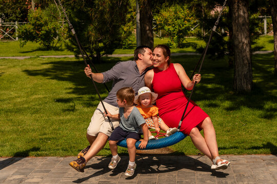 Father Kissing Mother Beside Children on Playground Swing