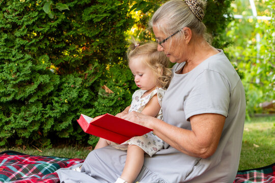 Grandmother Teaching Granddaughter With Red Book During Picnic