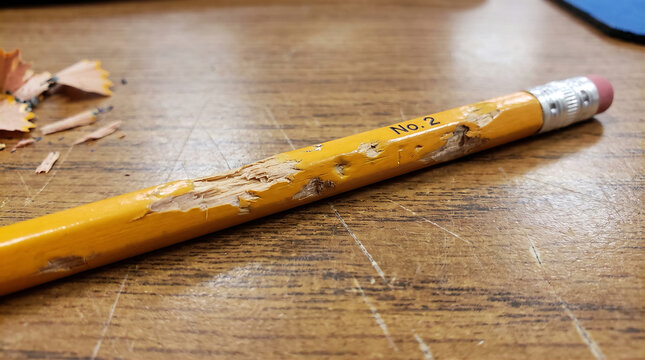 Chewed yellow pencil with eraser lying on a wooden desk with pencil shavings nearby