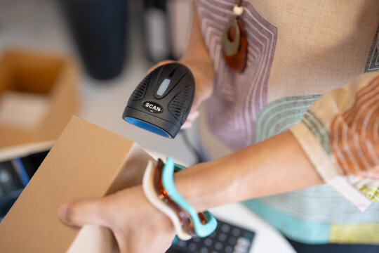 woman scanning product barcode with handheld scanner at handmade retail shop using technology small business management.