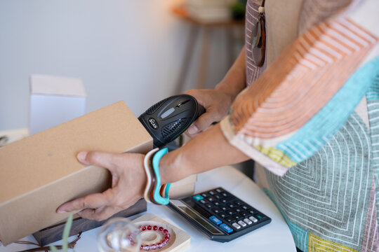 woman scanning product barcode with handheld scanner at handmade retail shop using technology small business management.