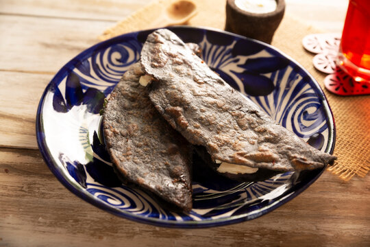 Mexican quesadillas made with blue corn tortillas filled with melted cheese and mushrooms served on a traditional plate and a glass of red hibiscus water (agua de jamaica) in the background.