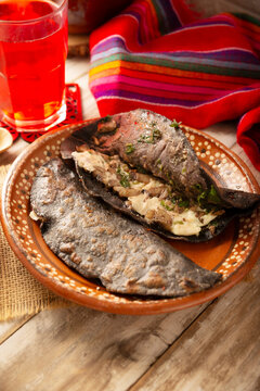 Mexican quesadillas made with blue corn tortillas filled with melted cheese and mushrooms served on a rustic clay plate and a glass of red hibiscus water (agua de jamaica) in the background.