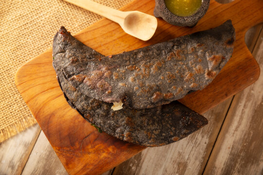 Mexican quesadillas made with blue corn tortillas filled with melted cheese and mushrooms served on a wooden cutting board.