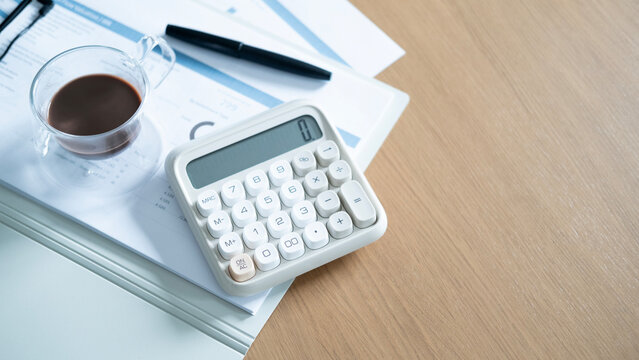 Calculator and coffee on financial reports with copy space on wooden desk. Business accounting, budgeting, financial planning and investment analysis concept.