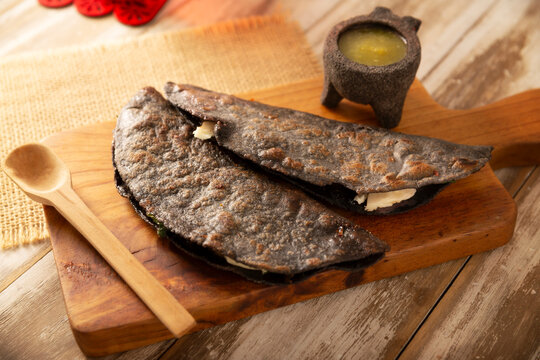 Mexican quesadillas made with blue corn tortillas filled with melted cheese and mushrooms served on a wooden cutting board.