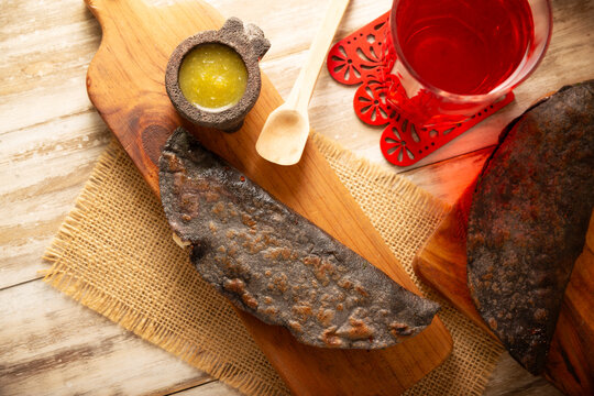 Mexican quesadillas made with blue corn tortillas filled with melted cheese and mushrooms served on a wooden cutting board and a glass of red hibiscus water (agua de jamaica) in the background.