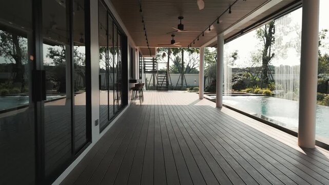 Perspective view of a spacious covered outdoor terrace with composite wood decking, ceiling fans, and glass sliding doors adjoining a swimming pool in a luxury Chiang Mai villa.