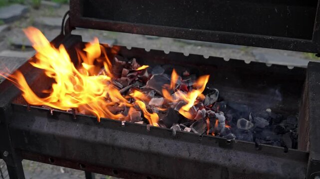 Golden flickers of fire consume pieces of coal within a rustic iron brazier as evening approaches, creating a warm atmosphere for cooking outdoors under the twilight sky.