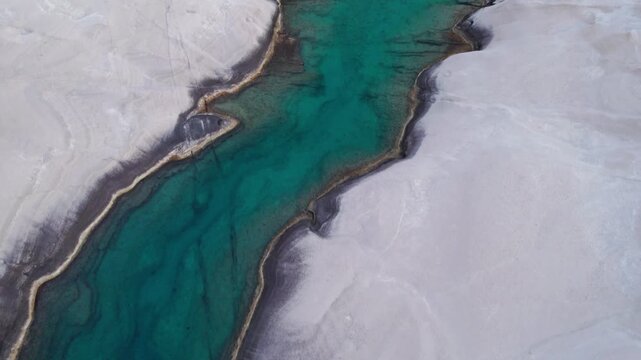 Top-down drone view of a swimmer in the turquoise sea canyon at Sarakiniko Beach, Milos. A famous Greek lunar-like landscape of white volcanic rock