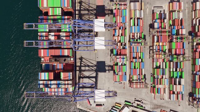Impressive top-down aerial view of a large cargo ship maneuvering into position at a bustling container port, with gantry cranes ready for loading and unloading freight for global trade
