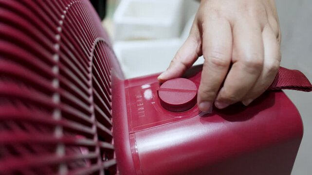 Close Up of Hand Turning Switch Knob on Red Electric Fan