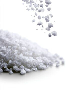 White coarse salt crystals falling and piling up on a smooth white surface with a bright background.